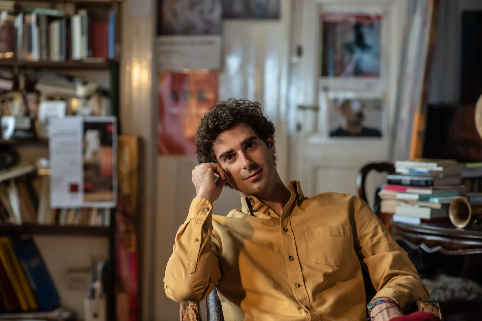 Luca Sacher seduto nello studio, camicia gialla, fra libri e quadri