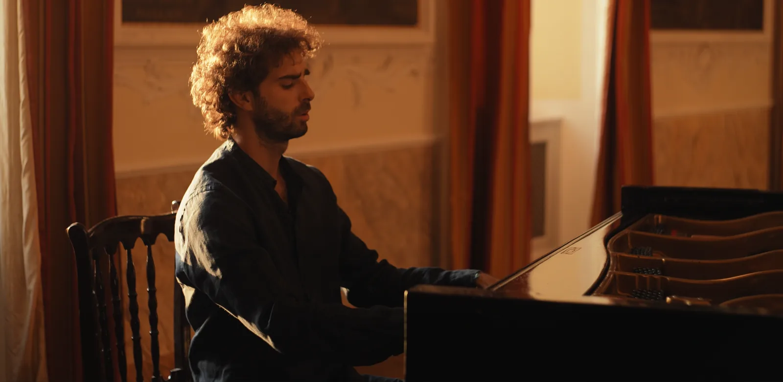 Luca Sacher al pianoforte a coda in una sala calda, la luce dalla finestra