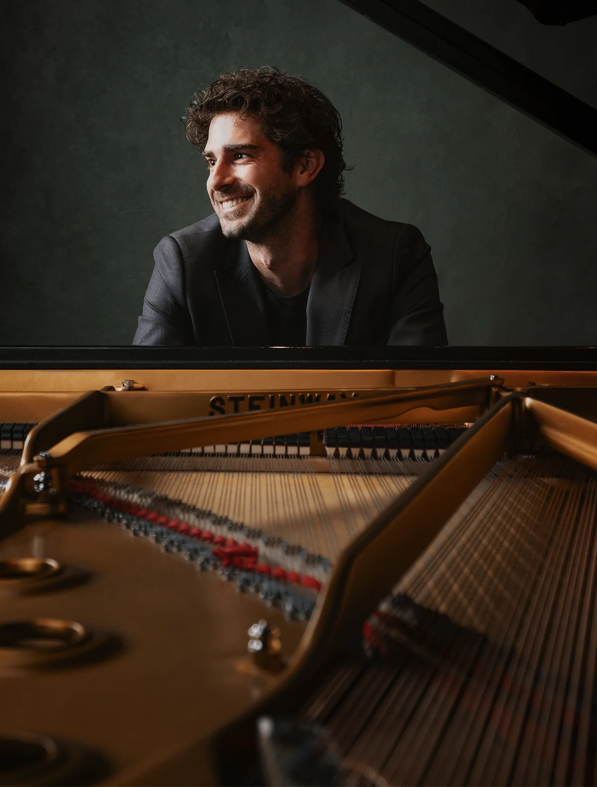 Luca Sacher sorride seduto al pianoforte, sul palco scuro