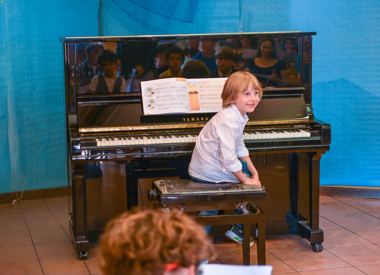 Un allievo felice dopo la sua esibizione al saggio di giugno, seduto al pianoforte davanti al pubblico